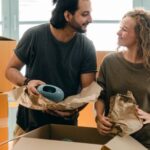 Real Estate Success - Multiethnic couple packing ceramic belongings in parchment before relocation